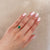 Close-up of a hand wearing the Dewlight Emerald Engagement Ring in 14k white gold, on a polished band.