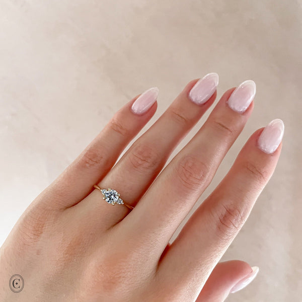 Alternative view of Close-up of a hand wearing the You, Me & Magic Round Cut Three Stone Engagement Ring in 14k white gold, on a polished band.